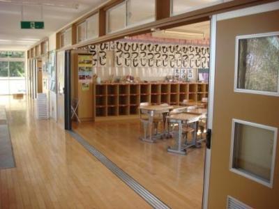 教室の後ろに「ひつじ」と書かれた書道が飾られ、扉が全部開かれろうかと一体になっている、地域活動室の一室の写真